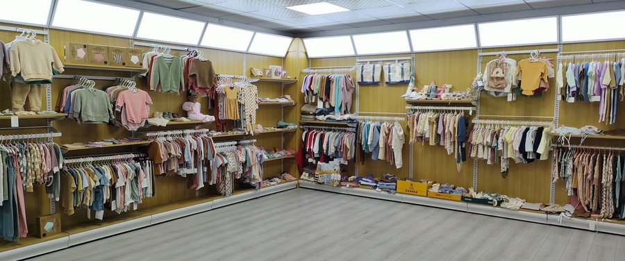 The Aston Garment showroom in Xinxiang, Henan — racks of finished baby and infant garments sorted by colour direction